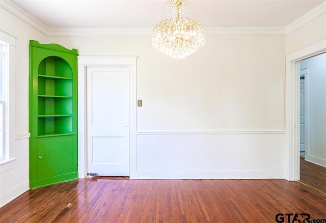 empty room with a notable chandelier, dark hardwood / wood-style flooring, and ornamental molding