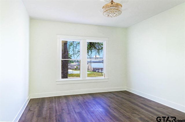 spare room with a notable chandelier, dark hardwood / wood-style floors, and a water view