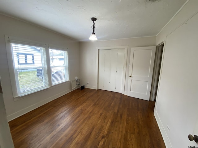 unfurnished bedroom with a closet, baseboards, and dark wood-style flooring