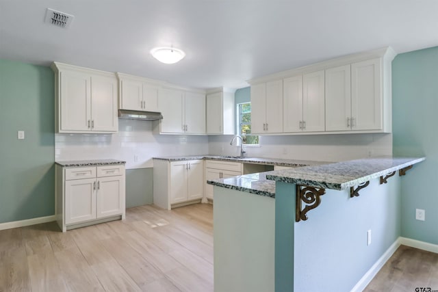 kitchen featuring white cabinets, a kitchen bar, light wood-type flooring, and kitchen peninsula