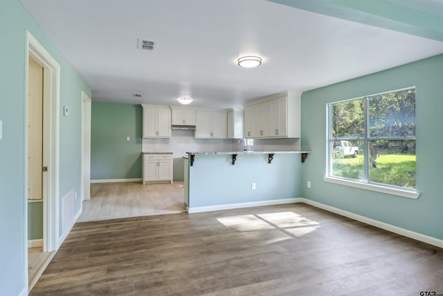 kitchen featuring a kitchen bar, kitchen peninsula, light stone counters, light hardwood / wood-style flooring, and white cabinets