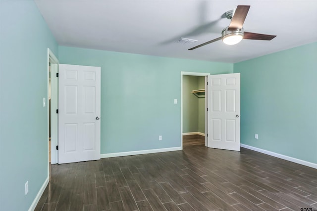 unfurnished bedroom with a walk in closet, ceiling fan, a closet, and dark wood-type flooring