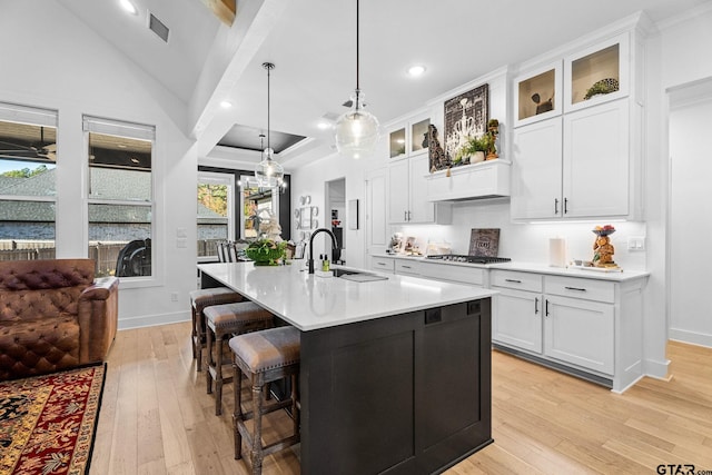 kitchen featuring white cabinets, sink, an island with sink, decorative light fixtures, and light hardwood / wood-style floors