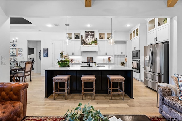 kitchen with a kitchen island with sink, pendant lighting, stainless steel appliances, and light hardwood / wood-style floors