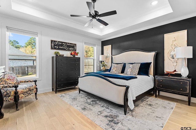 bedroom with ceiling fan, light wood-type flooring, crown molding, and a tray ceiling