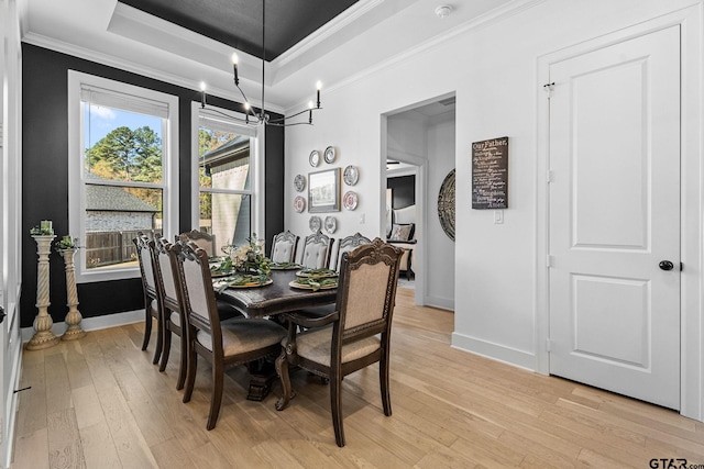 dining space featuring a tray ceiling, a chandelier, light hardwood / wood-style floors, and ornamental molding