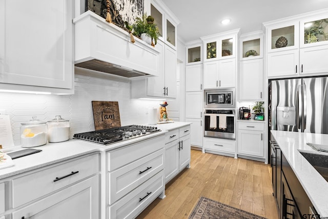 kitchen with light stone countertops, white cabinets, stainless steel appliances, and light hardwood / wood-style floors