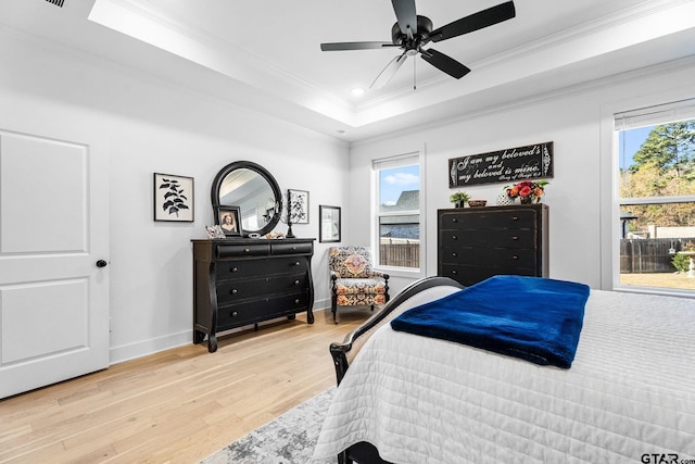 bedroom with ceiling fan, light wood-type flooring, crown molding, and a tray ceiling