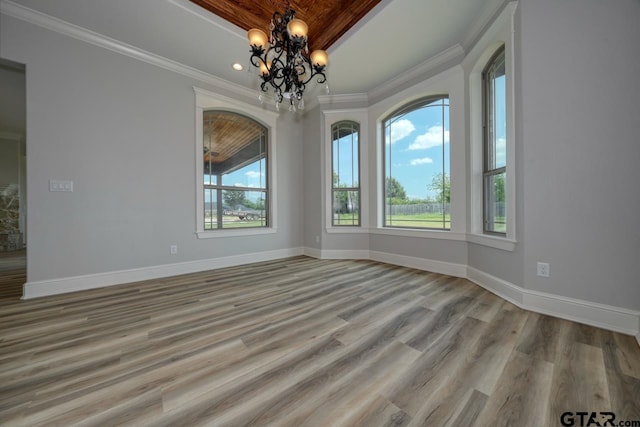 empty room with a notable chandelier, light wood-type flooring, and crown molding