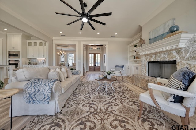 living room featuring french doors, ornamental molding, ceiling fan with notable chandelier, a premium fireplace, and light hardwood / wood-style floors