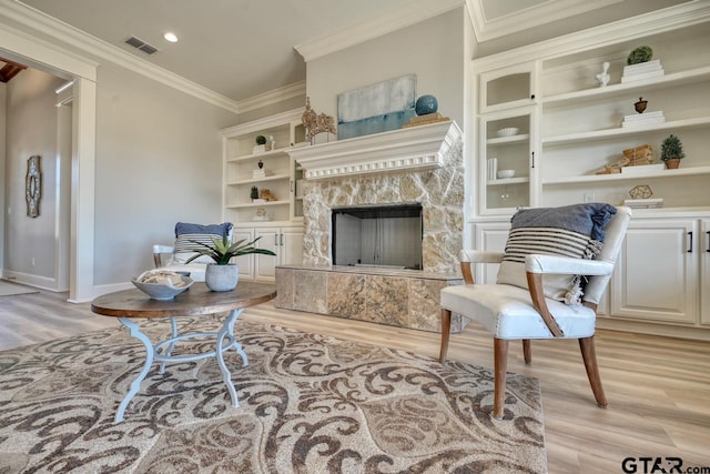 living room with crown molding, a fireplace, built in features, and light wood-type flooring