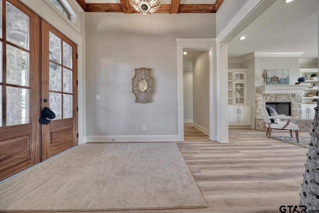 entryway with french doors, a fireplace, ornamental molding, beamed ceiling, and light hardwood / wood-style floors