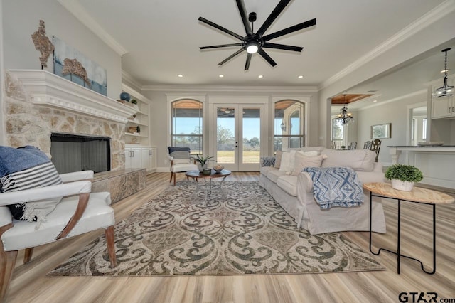 living room featuring ceiling fan with notable chandelier, light wood-type flooring, crown molding, and french doors