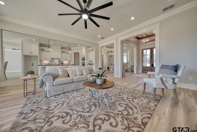 living room featuring light hardwood / wood-style flooring, ceiling fan with notable chandelier, french doors, and ornamental molding