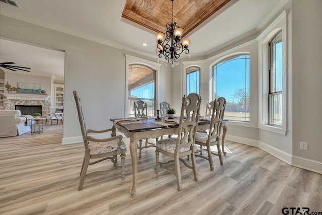 dining room featuring ceiling fan with notable chandelier, a raised ceiling, a stone fireplace, crown molding, and light wood-type flooring