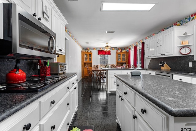 kitchen featuring dishwashing machine, tasteful backsplash, white cabinets, black cooktop, and kitchen peninsula