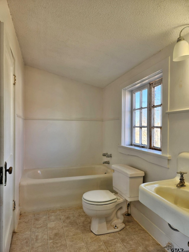 bathroom featuring a bathing tub, tile patterned floors, a textured ceiling, and toilet