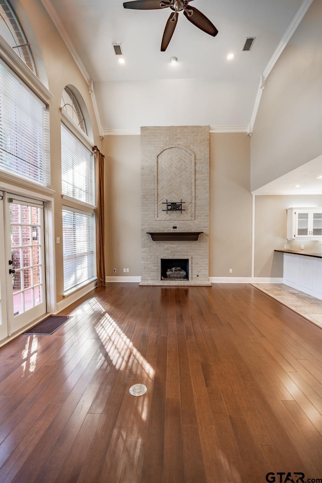 unfurnished living room with a large fireplace, vaulted ceiling, ceiling fan, crown molding, and hardwood / wood-style floors