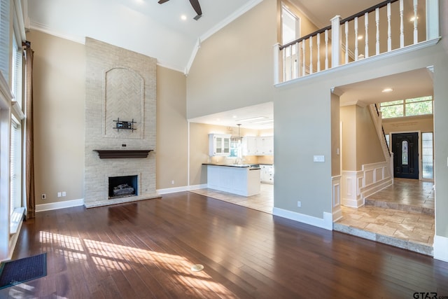 unfurnished living room featuring crown molding, wood-type flooring, a fireplace, and a high ceiling