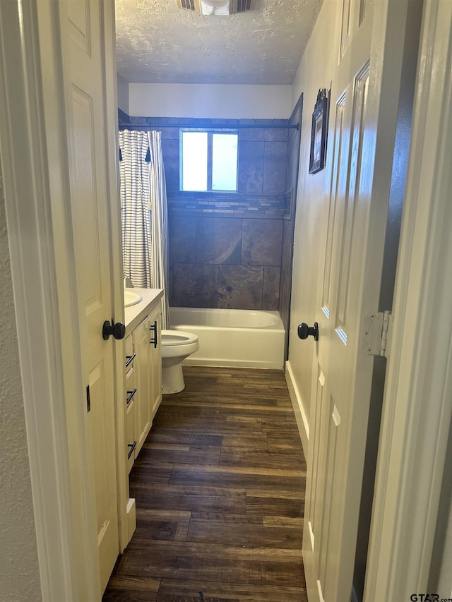 full bathroom featuring wood-type flooring, tiled shower / bath combo, vanity, toilet, and a textured ceiling