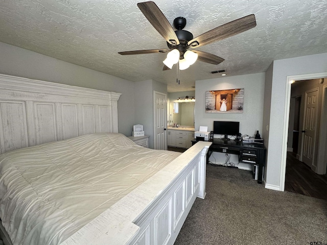 bedroom featuring ceiling fan, connected bathroom, a textured ceiling, and dark carpet