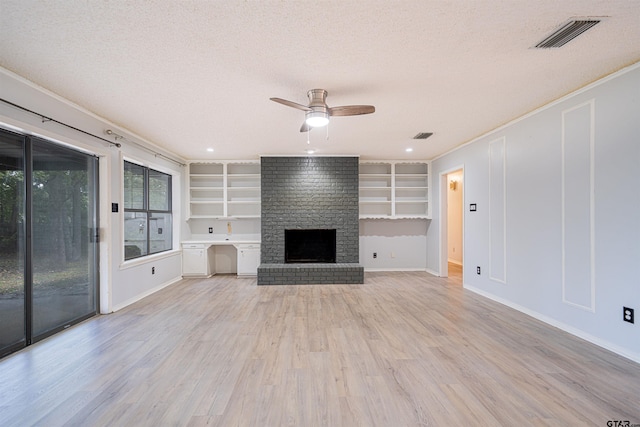 unfurnished living room with a brick fireplace, built in shelves, a textured ceiling, ceiling fan, and light wood-type flooring