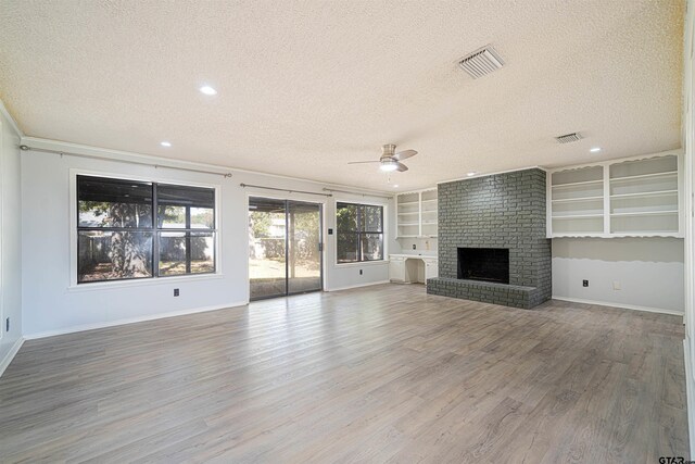 unfurnished living room with built in shelves, hardwood / wood-style flooring, a textured ceiling, ceiling fan, and a fireplace