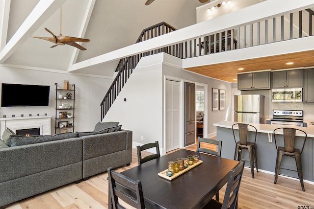 dining space with high vaulted ceiling, beam ceiling, ceiling fan, and light hardwood / wood-style flooring