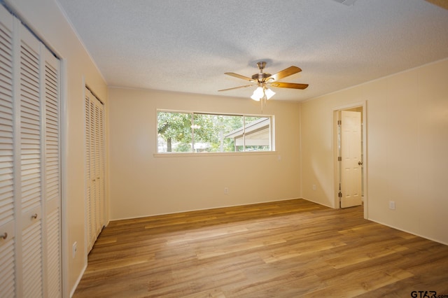 unfurnished bedroom featuring a textured ceiling, light hardwood / wood-style floors, ceiling fan, and multiple closets