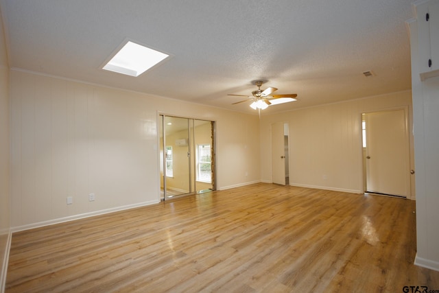 spare room featuring ceiling fan, light hardwood / wood-style floors, crown molding, and a skylight