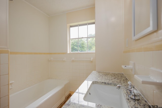 bathroom with a washtub, a textured ceiling, vanity, tile walls, and ornamental molding