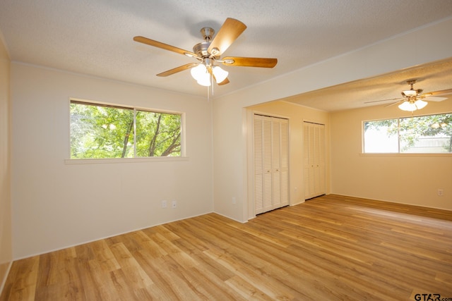 unfurnished bedroom with a textured ceiling, ceiling fan, light hardwood / wood-style flooring, and multiple closets