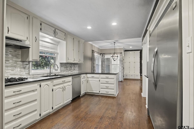 kitchen with dark wood-type flooring, sink, tasteful backsplash, kitchen peninsula, and stainless steel appliances