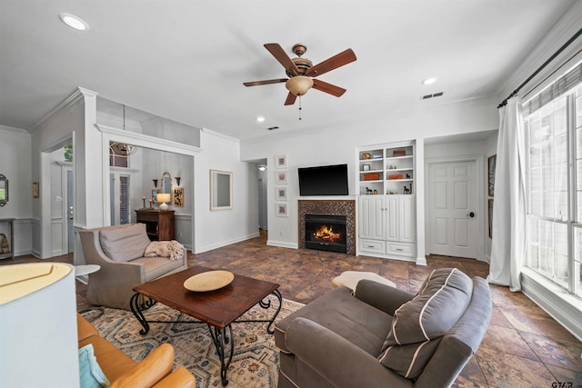 living room with built in shelves, a wealth of natural light, a tiled fireplace, and crown molding