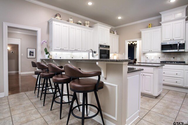 11208 Marsh Wren Cir, Flint, TX 75762 - kitchen featuring appliances with stainless steel finishes, a kitchen breakfast bar, decorative backsplash, ornamental molding, and white cabinetry