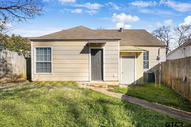 rear view of property featuring a fenced backyard, a lawn, central AC, and roof with shingles