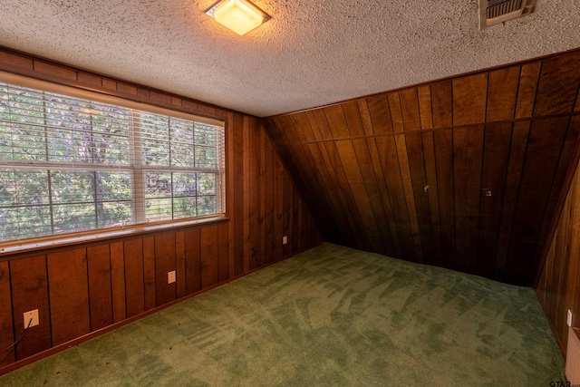 carpeted spare room with wood walls, lofted ceiling, and a textured ceiling