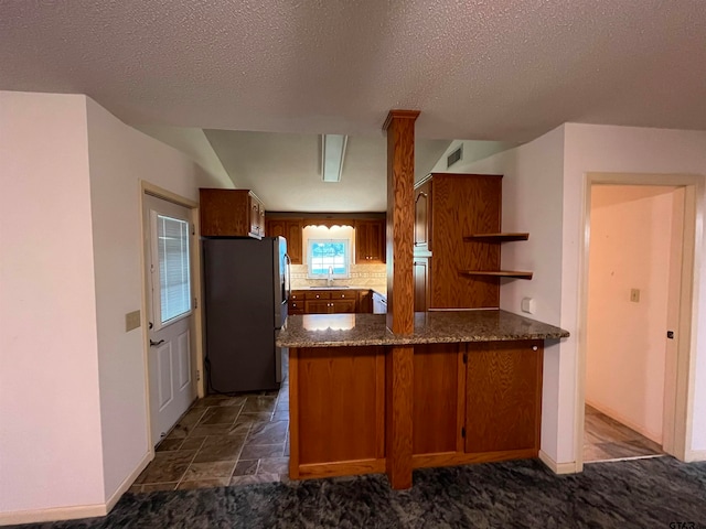 kitchen featuring a textured ceiling, stainless steel refrigerator, decorative backsplash, sink, and kitchen peninsula