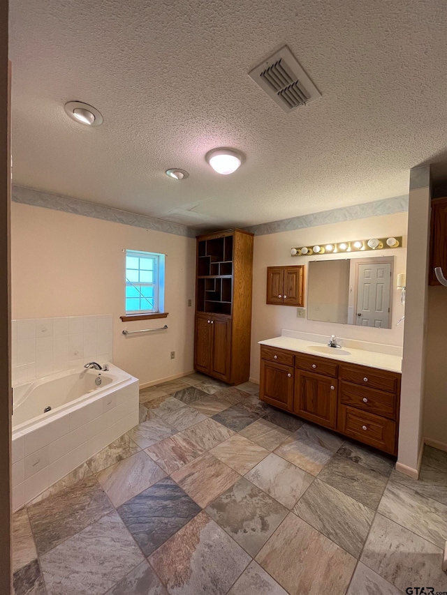 bathroom featuring tiled bath, vanity, and a textured ceiling