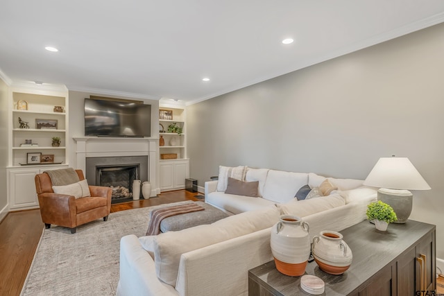 living room featuring built in shelves, ornamental molding, and light hardwood / wood-style flooring