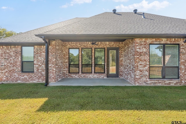 rear view of house featuring brick siding, a shingled roof, a lawn, and a patio area