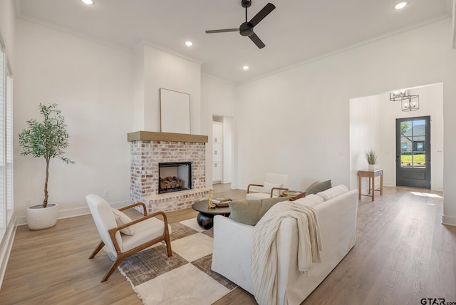 living area with ceiling fan with notable chandelier, ornamental molding, and light wood finished floors