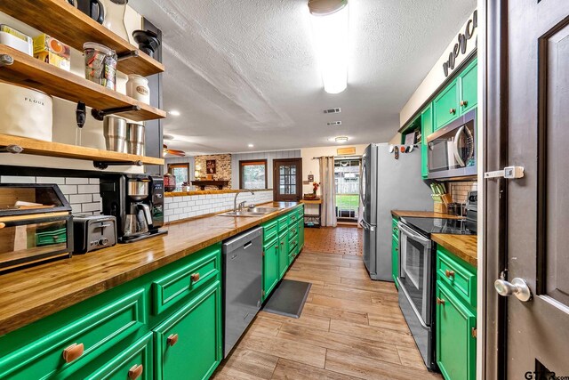 kitchen with decorative backsplash, wood counters, stainless steel appliances, open shelves, and a sink