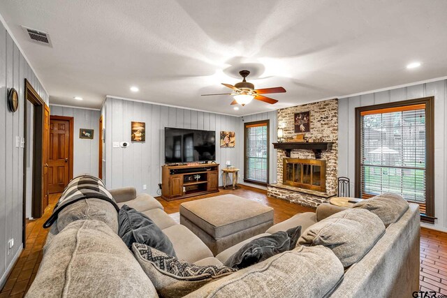 living area with brick floor, crown molding, visible vents, a ceiling fan, and a large fireplace