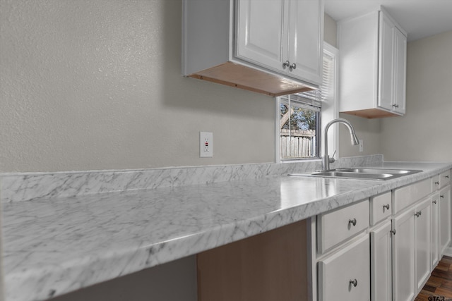 kitchen with light stone counters, white cabinetry, and a sink