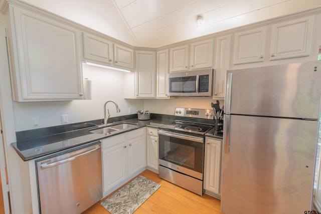 kitchen featuring vaulted ceiling, sink, light hardwood / wood-style flooring, and appliances with stainless steel finishes