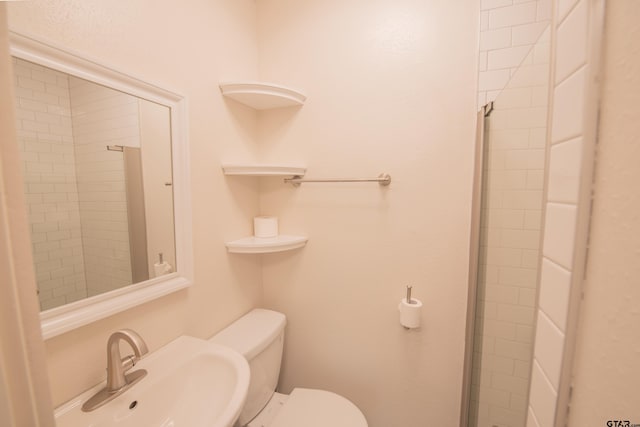 bathroom featuring a shower with door, sink, and toilet