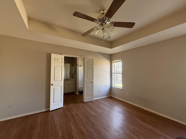 unfurnished bedroom featuring ceiling fan, a tray ceiling, dark wood-type flooring, and baseboards