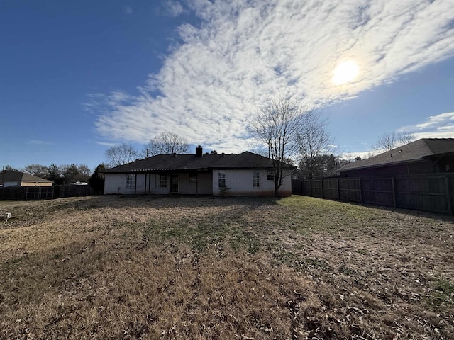 rear view of house featuring a yard, a chimney, and a fenced backyard