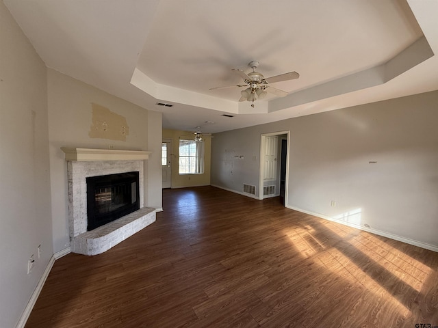 unfurnished living room featuring visible vents, baseboards, wood finished floors, a tray ceiling, and a brick fireplace